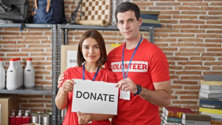 Photo for Man and woman volunteers standing together holding paper with donate message at charity center - Royalty Free Image