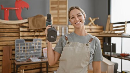 Photo for Smiling young woman holding a drill in a well-organized carpentry workshop - Royalty Free Image