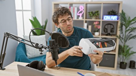 Hispanischer Mann untersucht ein VR-Headset in einem modernen Radiostudio, das auf Technik und Rundfunk hinweist.