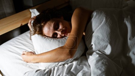 Foto de Una joven serena en apacible letargo, envuelta por ropa de cama suave en un ambiente acogedor dormitorio - Imagen libre de derechos
