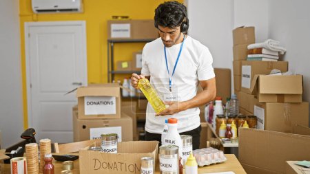 bel homme hispanique faisant du bénévolat à l'intérieur dans un centre de dons, organisant des articles alimentaires dans une pièce.