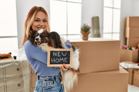 Photo for Young caucasian woman holding blackboard hugging dog at new home - Royalty Free Image