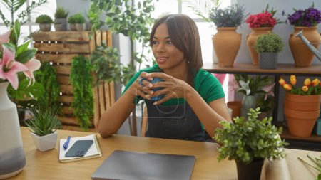 Téléchargez les photos : Femme afro-américaine profite d'une pause café au milieu de plantes d'intérieur vibrantes dans un cadre confortable magasin de fleurs - en image libre de droit