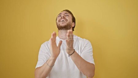 Foto de Joven hispano sonriendo confiado aplaudiendo sobre aislado fondo amarillo - Imagen libre de derechos