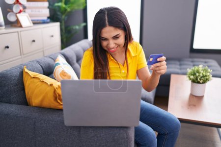 Téléchargez les photos : Jeune belle femme arabe utilisant ordinateur portable et carte de crédit assis sur le canapé à la maison - en image libre de droit