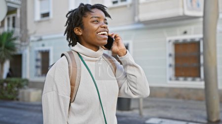 Photo for Young black woman with dreadlocks talking on a smartphone on an urban city street - Royalty Free Image