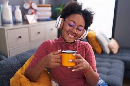 Foto de Mujer afroamericana escuchando música tomando café en casa - Imagen libre de derechos