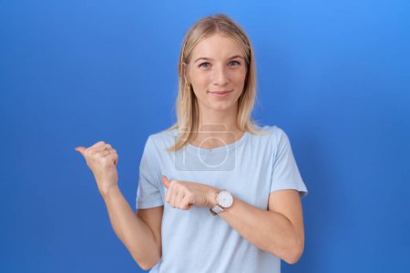 Photo for Young caucasian woman wearing casual blue t shirt pointing to the back behind with hand and thumbs up, smiling confident - Royalty Free Image
