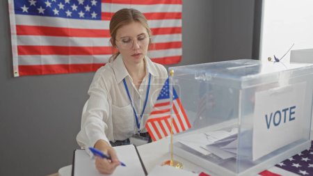 Foto de Una joven supervisa un proceso electoral de EE.UU. en el interior, por la bandera americana. - Imagen libre de derechos