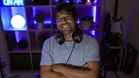 Handsome bearded man with headphones smiling in a modern gaming room at night