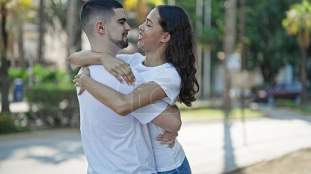 Téléchargez les photos : Couple confiant et beau, embrassant et souriant joyeusement dans un parc ensoleillé, exprimant amour et bonheur tout en profitant d'un style de vie décontracté et en plein air. - en image libre de droit