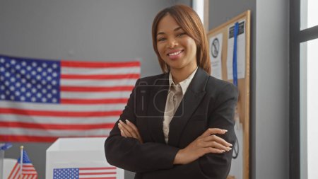 Photo for Confident african american woman in business attire with crossed arms, standing in a college electoral center with usa flags. - Royalty Free Image