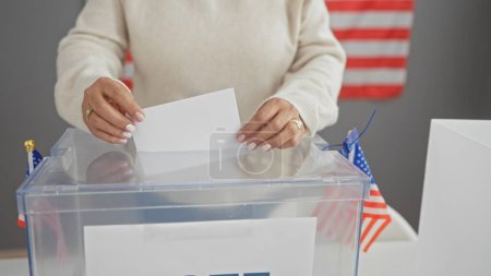 Téléchargez les photos : Une femme vote dans un centre électoral américain, avec un drapeau américain en arrière-plan. - en image libre de droit