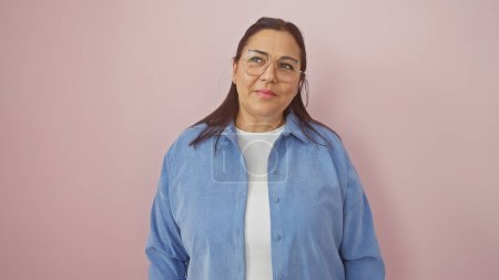 Photo for Mature hispanic woman in a blue shirt, smiling against a pink isolated background. - Royalty Free Image