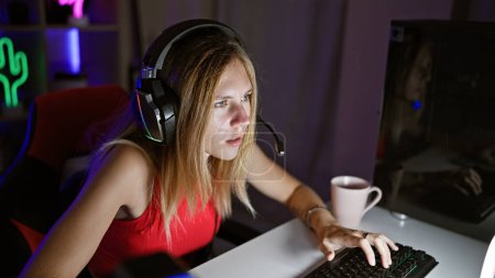 Konzentrierte junge Frau mit Kopfhörern am Computer in einem dunklen Spielzimmer