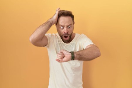 Photo for Middle age man with beard standing over yellow background looking at the watch time worried, afraid of getting late - Royalty Free Image