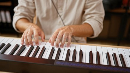 A close-up of a man's hands playing a keyboard at an indoor studio showcasing his musical talent.