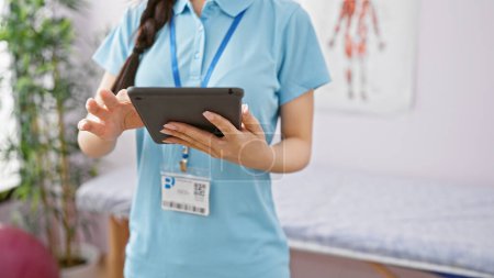Asiatische Gesundheitsexpertin mit Tablette in Klinik-Interieur, verkörpert moderne medizinische Praxis.