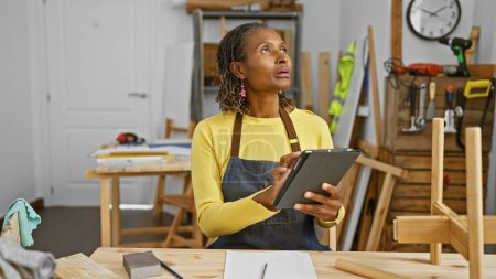 Photo for African american woman using a tablet in a carpentry workshop looking focused and entrepreneurial - Royalty Free Image