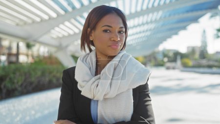 African american woman in business attire poses confidently outdoors in a modern city park setting during the daytime.