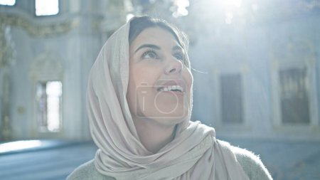 Téléchargez les photos : Jeune femme adulte portant un hijab regardant vers le haut à l'intérieur d'une mosquée istanbul ornée, transmettant un sentiment d'émerveillement. - en image libre de droit