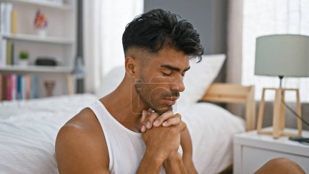 Photo for Hispanic man praying in a modern bedroom, showcasing spirituality and a tranquil lifestyle at home. - Royalty Free Image