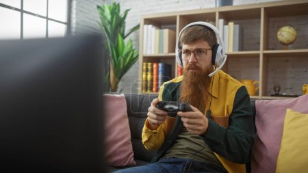 Photo for Focused man with beard and glasses playing video games indoors, showcasing a cozy lifestyle and entertainment. - Royalty Free Image