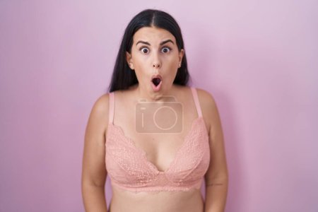 Foto de Mujer hispana joven con sujetador rosa asustada y conmocionada con sorpresa y expresión asombrada, miedo y cara emocionada. - Imagen libre de derechos