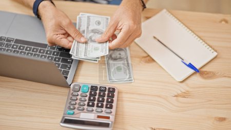 Photo for Man counts dollars near calculator, laptop, and notebook on wooden office desk. - Royalty Free Image