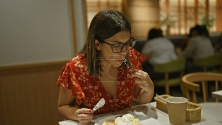 Belle femme hispanique dans des lunettes savourant une crêpe japonaise moelleuse dans un café confortable, indulgence matinale d'un dessert sucré fait maison