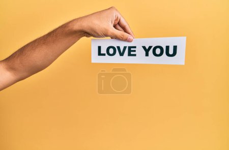 Hand of caucasian man holding paper with love you message over isolated yellow background