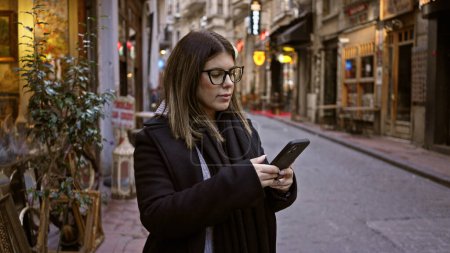 Téléchargez les photos : Femme adulte naviguant smartphone sur la rue historique de Istanbul, mettant en valeur les voyages et la vie urbaine en Turquie. - en image libre de droit