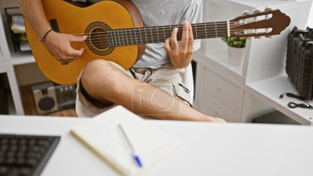 Foto de Joven hispano tocando una guitarra acústica en el interior, mostrando talento musical y creatividad. - Imagen libre de derechos