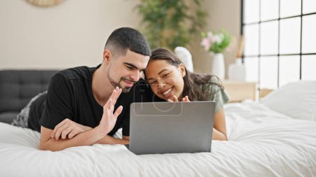 Photo for Adorable couple smiling and relaxing at home, lying in bed chatting and enjoying a lovely video call in their cosy, beautifully designed bedroom. - Royalty Free Image