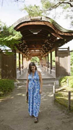 Schöne hispanische Frau, die Freude ausstrahlt, selbstbewusst stehend posiert und in die Kamera lächelt, während sie zu heian jingu in traditionellem Kyoto, Japan geht