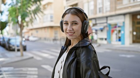 Téléchargez les photos : Une jeune femme brune aime la musique sur un casque tout en marchant dans une rue urbaine ensoleillée. - en image libre de droit