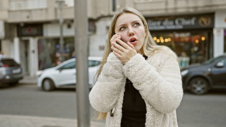Eine junge kaukasische Frau telefoniert auf einer Straße der Stadt und übermittelt Dringlichkeit oder Überraschung.