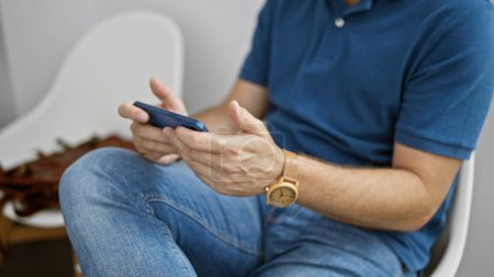 Foto de Hombre hispano maduro usando teléfono inteligente en una habitación interior moderna, usando ropa casual y un reloj de pulsera. - Imagen libre de derechos