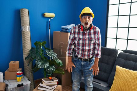 Shocked senior man with grey hair dons hardhat and safety glasses, showing a scared yet excited face at his new home, eliciting an expression of pure amazement and fear! wow, amazing turnaround!