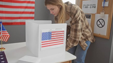 Foto de Mujer joven votando en una sala de colegio electoral interior de estados unidos, adornada con bandera americana. - Imagen libre de derechos