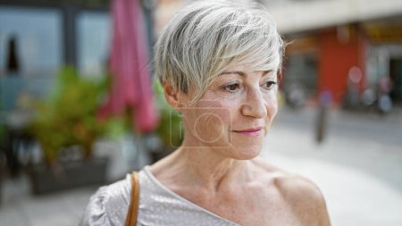 Foto de Una mujer hispana madura con el pelo gris corto se muestra en un hermoso retrato en un fondo de la calle de la ciudad. - Imagen libre de derechos