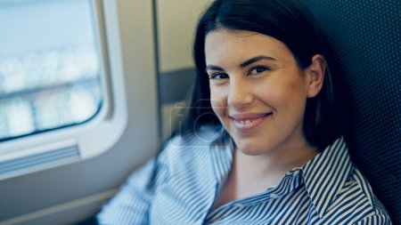 Foto de Joven hermosa mujer hispana sonriendo feliz sentado dentro de vagón de tren - Imagen libre de derechos