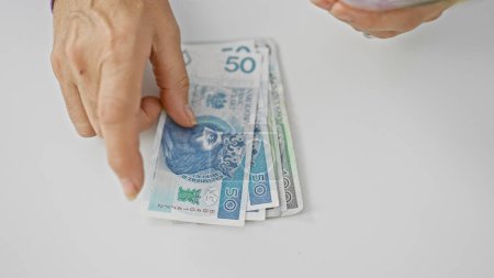 Una mujer madura cuenta los billetes de zloty polacos con un fondo blanco, lo que indica la gestión financiera y el ahorro.