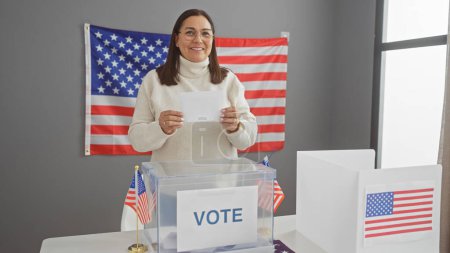 Mujer hispana madura votando en un centro electoral de EE.UU. con banderas americanas
