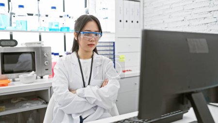 A young asian woman scientist confidently studies data on a computer in a modern laboratory.