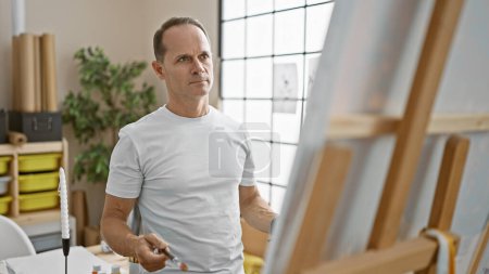 Photo for Handsome middle-aged hispanic man concentrating on drawing artwork in vibrant art studio - Royalty Free Image
