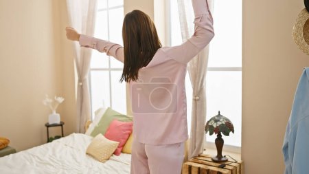 Photo for A young, brunette woman stretches after waking up in her sunny, cozy bedroom, setting a serene morning scene. - Royalty Free Image