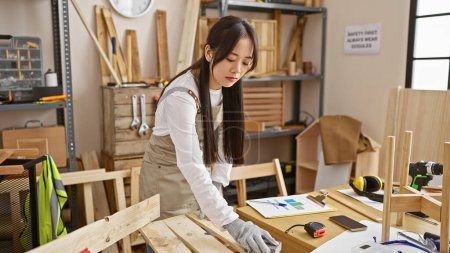 Foto de Una joven asiática trabaja meticulosamente en un taller de carpintería, rodeada de herramientas y madera. - Imagen libre de derechos