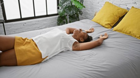 Foto de Mujer relajada acostada en una cama interior con acentos amarillos y plantas verdes. - Imagen libre de derechos