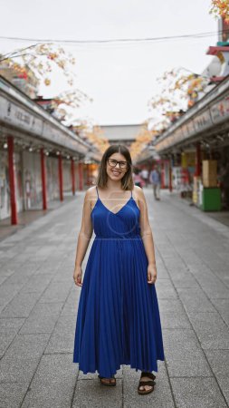 Joyeux belle femme hispanique dans des lunettes, posant avec un sourire confiant sur la rue nakamise, asakusa, tokyo